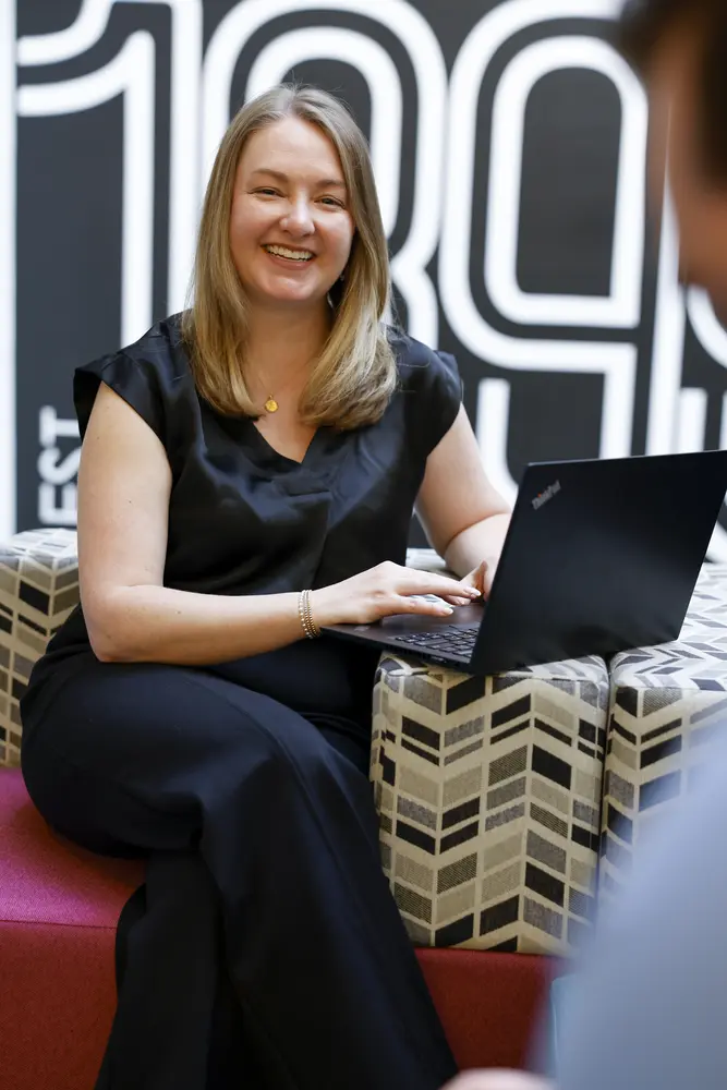 A Sonoco employee smiling during a conversation with a laptop on her lap in a modern office lounge.